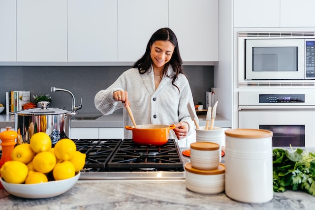 Smiling person stirring an orange pot on a stove in a clean kitchen
